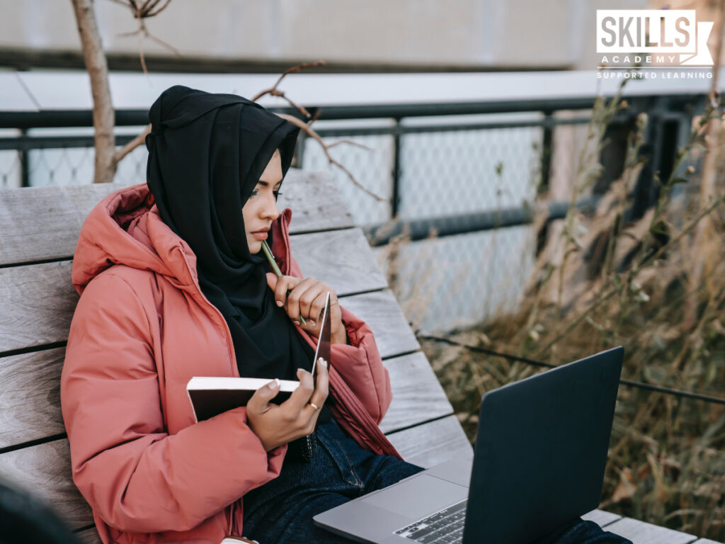Student holding a notebook and pen, reading from a laptop. Take a look at the benefits of studying matric online right here.