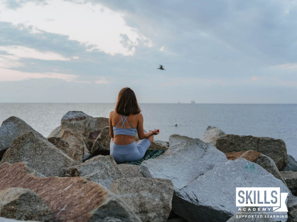 Girl meditating on rocks infront of the ocean. People skills to help you succeed in the work place.