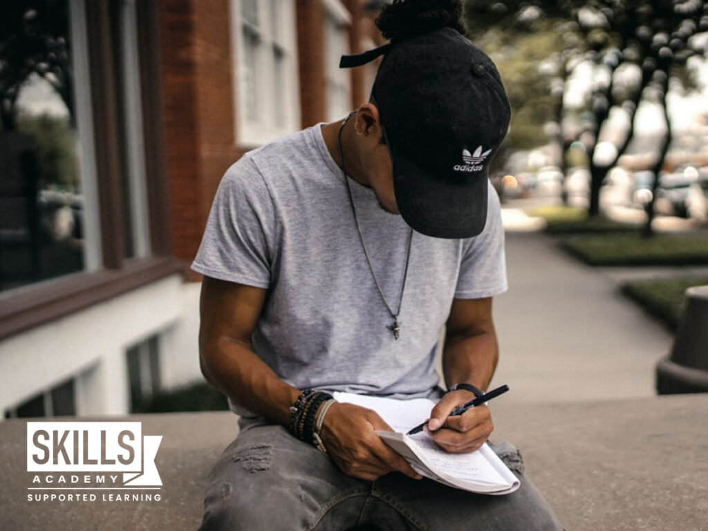 Guy sitting outside writing in his notebook while he looks down. Useful Tips When Writing Assignments