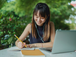 Girl writing on notebook behind laptop. How to Write a Strong Conclusion for Your Essays