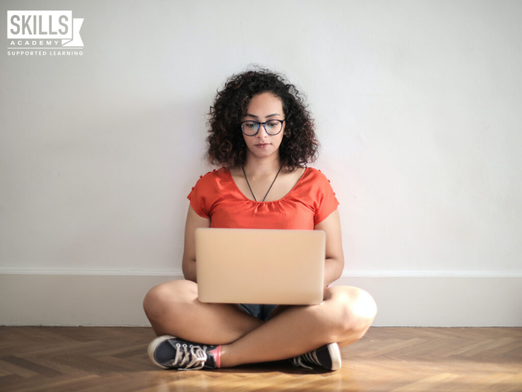 Girl sitting against a wall on her laptop. Top Soft Skills Every Freelancer Needs