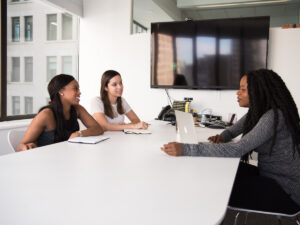 Three girls sitting and talking around the boardroom table. How to Know if you are Ready for a Promotion.