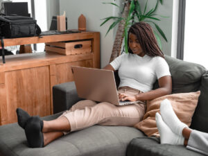 Student sitting on a couch with a laptop on her legs. Study ICB courses online and learn quality finance skills.