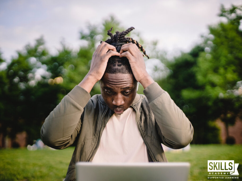 Student sitting outside with his laptop on a lawn with his hands on his head. What are your options if you failed the ICB exam? Find out right here.