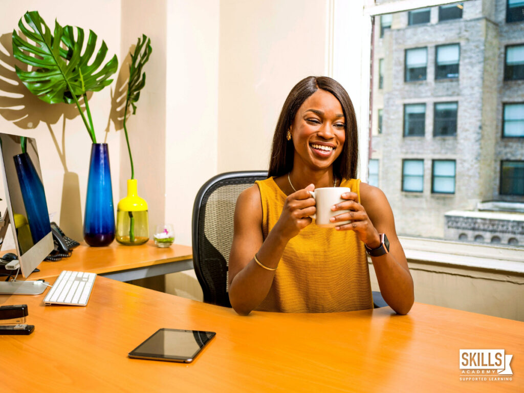Businesswoman sitting at a desk in her office drinking coffee. ICB qualifications.