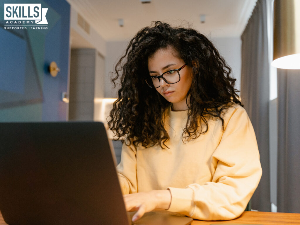 Student wearing a yellow sweatshirt typing on a laptop. Study accounting courses online and learn quality finance skills right at home.
