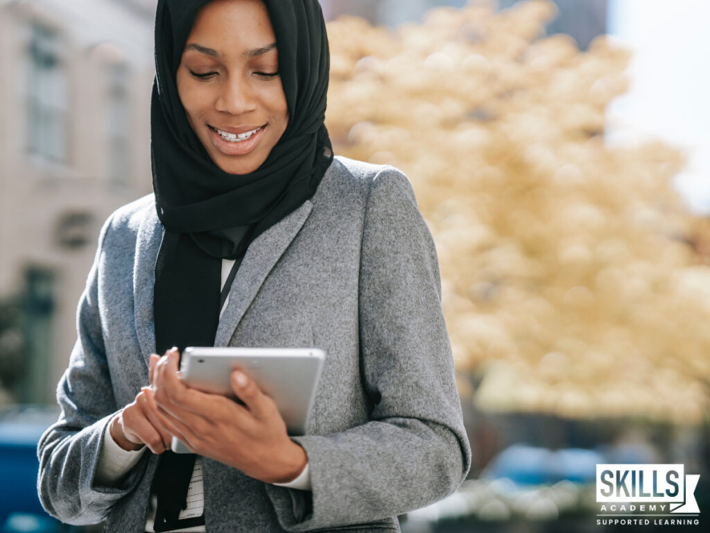 Woman smiling, while standing outside and using a tablet. Learn quality office management skills when you study office administration courses online.