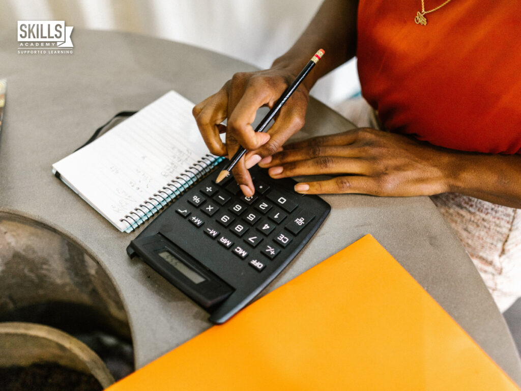 Bookkeeper doing calculations on a calculator with a pen in hand. Where to study bookkeeping online in South Africa.
