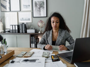 woman counting money at her desk. Why Study Bookkeeping With the ICB.