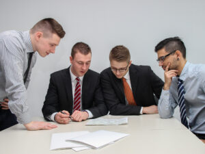 Four guys discussing over paperwork. How to Start a Career in Business Management.