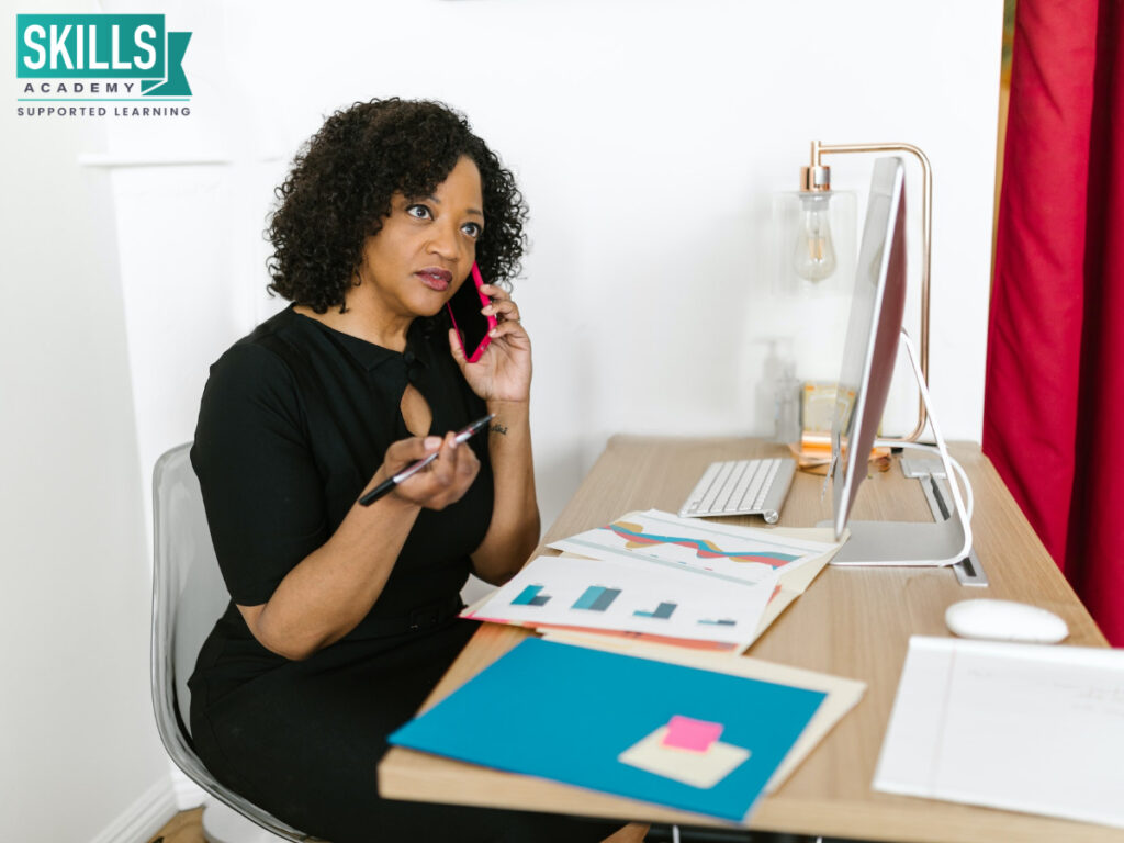 Office administrator talking on a phone while sitting at a desk. Wondering “is office administration a good career”? Find out here.